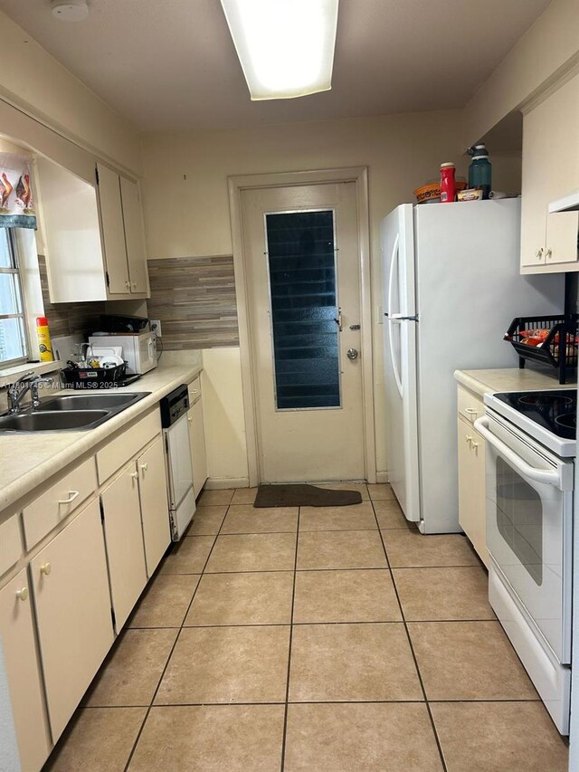 kitchen with white appliances, a sink, light countertops, light tile patterned floors, and white cabinets