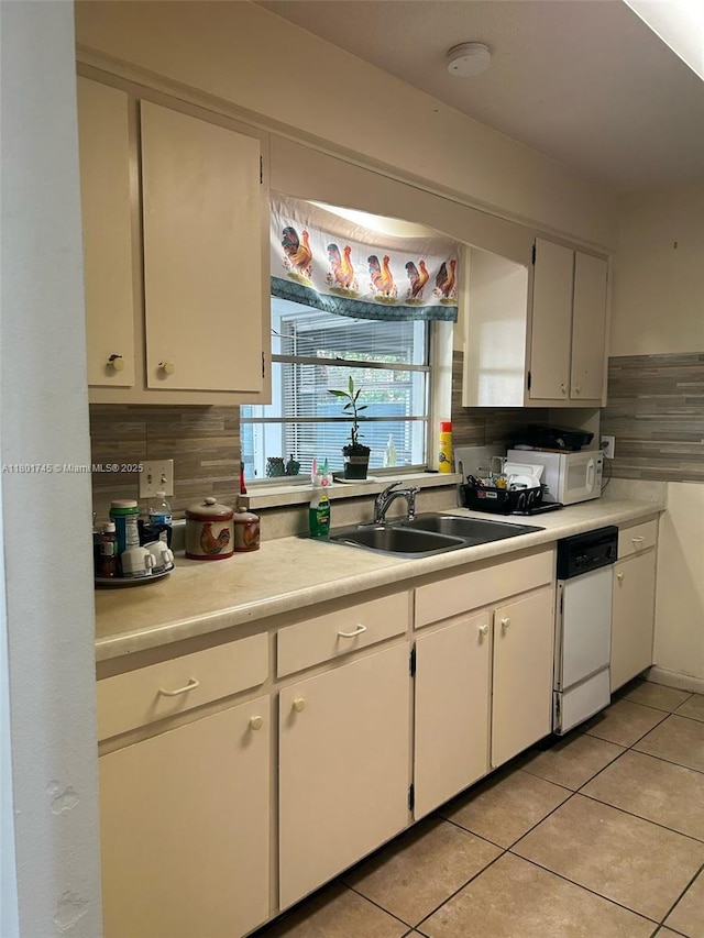 kitchen with a sink, decorative backsplash, white dishwasher, light countertops, and light tile patterned flooring