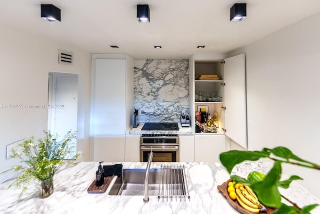 kitchen featuring stainless steel oven, white cabinetry, black stovetop, and light stone counters