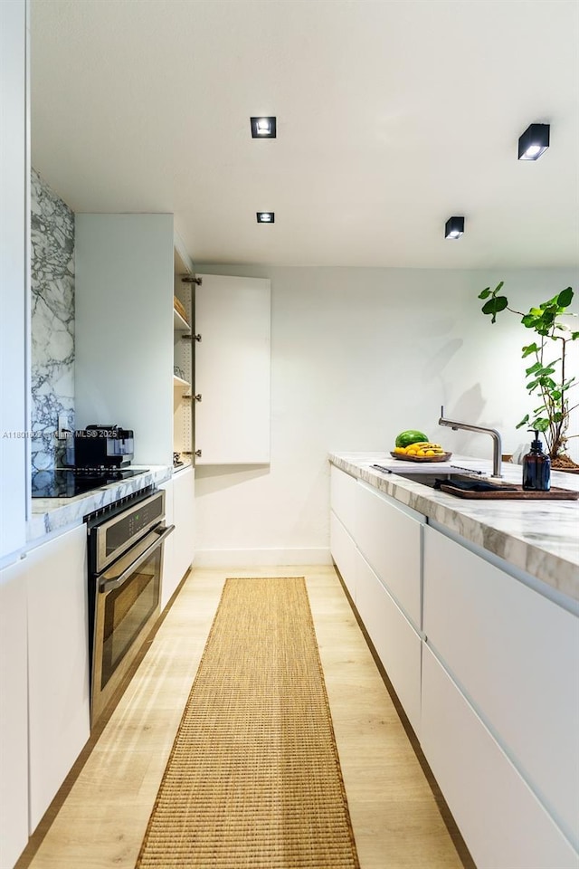 kitchen with stainless steel oven, white cabinetry, light countertops, light wood-type flooring, and open shelves