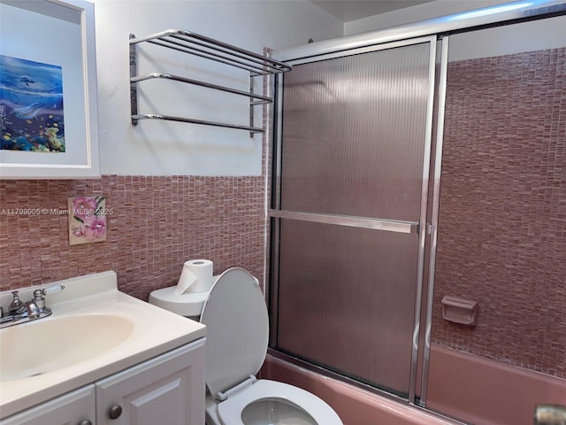 bathroom featuring tile walls, combined bath / shower with glass door, toilet, and vanity
