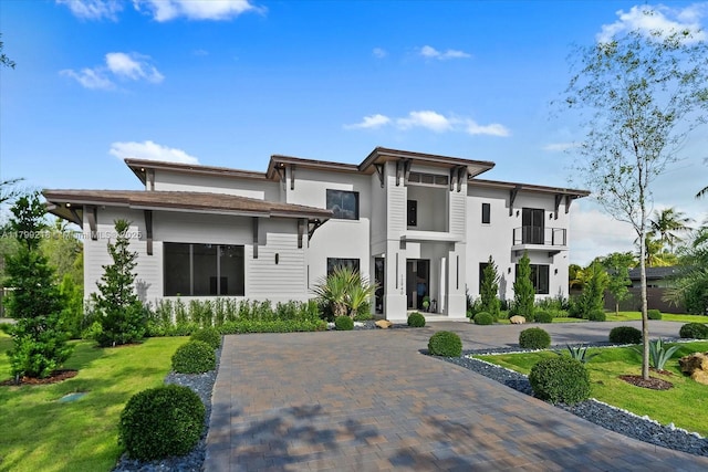 view of front of home featuring a balcony, stucco siding, and a front yard
