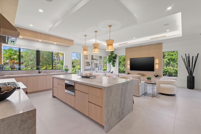 kitchen with light brown cabinetry, modern cabinets, light stone countertops, a raised ceiling, and open floor plan