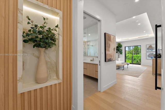 hallway with light wood-style flooring, a sink, recessed lighting, and baseboards