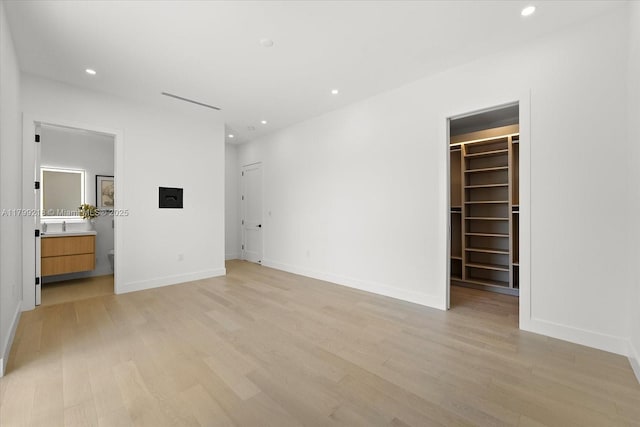 unfurnished bedroom featuring light wood-type flooring, a spacious closet, recessed lighting, and baseboards