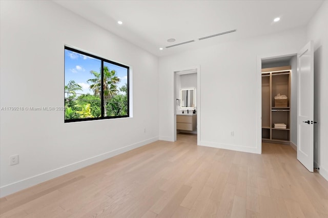 unfurnished bedroom with a walk in closet, light wood finished floors, baseboards, recessed lighting, and connected bathroom