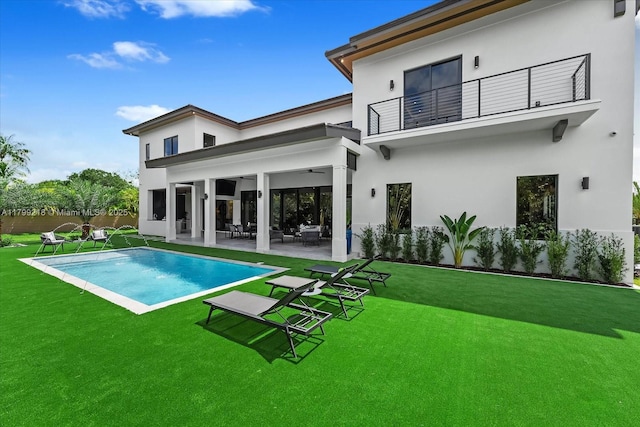 rear view of property with a balcony, a patio area, ceiling fan, a yard, and stucco siding