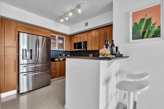 kitchen featuring stainless steel appliances, brown cabinetry, tasteful backsplash, a peninsula, and a textured ceiling