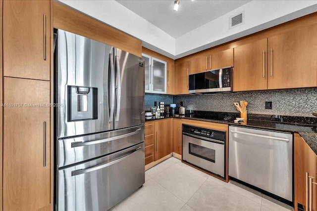 kitchen with appliances with stainless steel finishes, tasteful backsplash, light tile patterned floors, and dark stone countertops