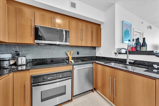 kitchen featuring appliances with stainless steel finishes, a sink, dark stone countertops, and backsplash