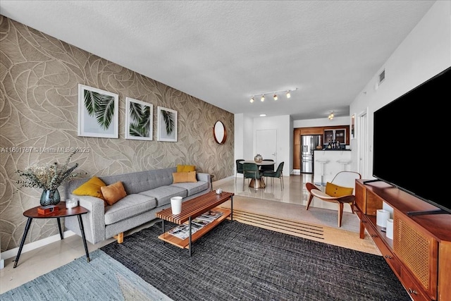 living room featuring wallpapered walls, baseboards, and a textured ceiling