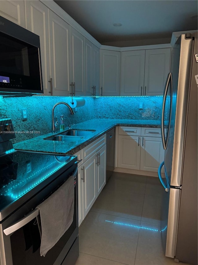 kitchen with appliances with stainless steel finishes, a sink, light tile patterned flooring, and white cabinetry