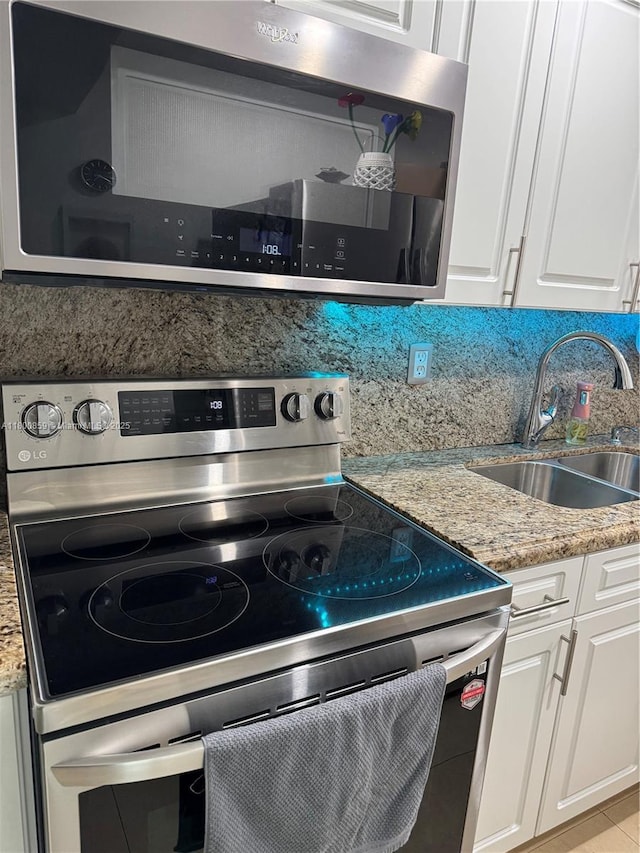 kitchen featuring appliances with stainless steel finishes, a sink, white cabinets, and light stone countertops