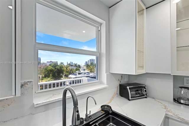 137 Golden Isles Dr Unit 305, Hallandale Beach, FL 33009 - kitchen featuring glass insert cabinets, white cabinetry, light stone counters, and a city view