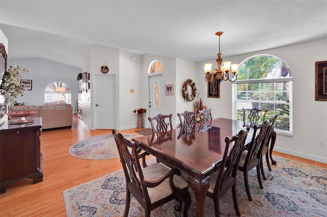 dining room with a chandelier, plenty of natural light, light wood-type flooring, baseboards, and lofted ceiling