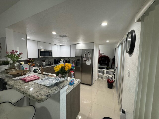8098 NW 99th Ter, Hialeah Gardens, FL 33016 - kitchen with stainless steel appliances, a peninsula, backsplash, white cabinets, and modern cabinets