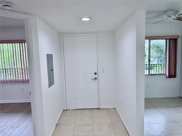 foyer entrance featuring electric panel, a ceiling fan, a textured ceiling, baseboards, and light tile patterned floors