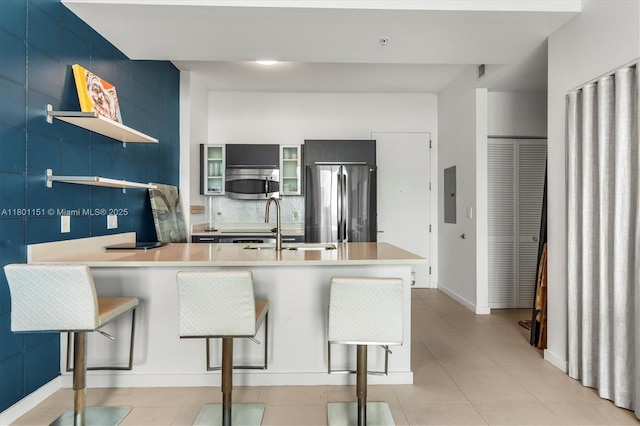 kitchen featuring open shelves, appliances with stainless steel finishes, a sink, a breakfast bar, and a peninsula