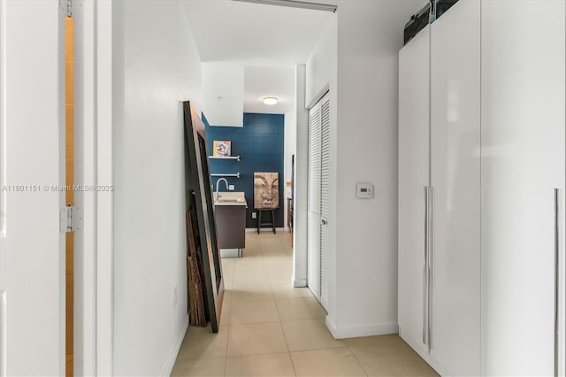 corridor with light tile patterned flooring, a sink, and baseboards