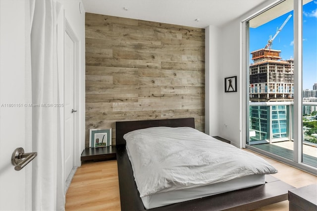 bedroom with a wall of windows, access to outside, light wood-type flooring, wooden walls, and an accent wall