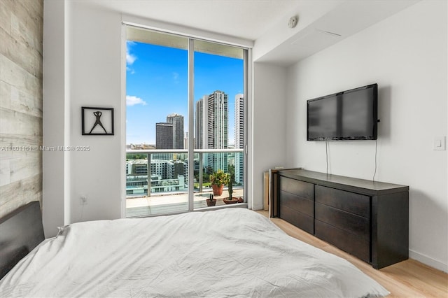 bedroom with expansive windows, wood finished floors, and baseboards