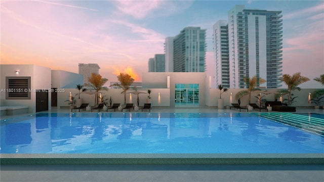 pool at dusk with an outdoor pool and a city view