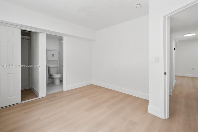 unfurnished bedroom with light wood finished floors, baseboards, a closet, and ensuite bath