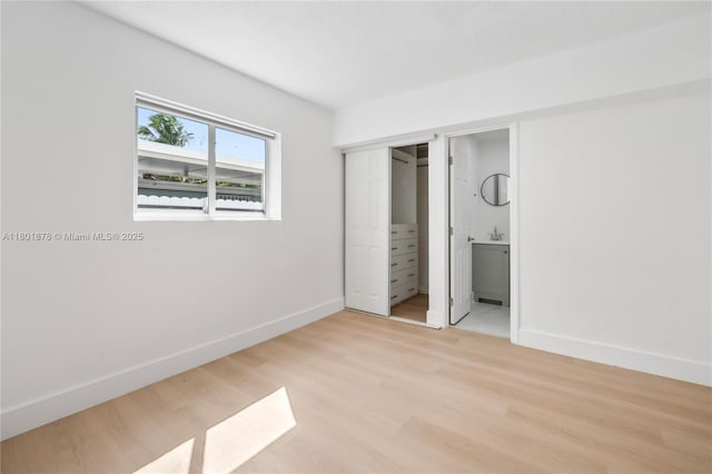 unfurnished bedroom with baseboards, light wood-type flooring, and ensuite bathroom