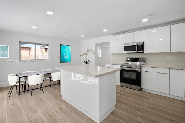 kitchen with appliances with stainless steel finishes, wood tiled floors, recessed lighting, white cabinets, and light countertops