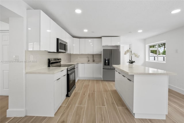kitchen featuring stainless steel appliances, modern cabinets, light wood-style flooring, a center island, and white cabinets