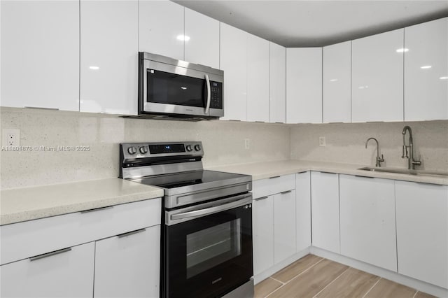 kitchen featuring appliances with stainless steel finishes, a sink, white cabinets, and modern cabinets