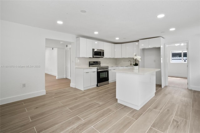 kitchen featuring stainless steel appliances, light wood-type flooring, light countertops, baseboards, and white cabinetry