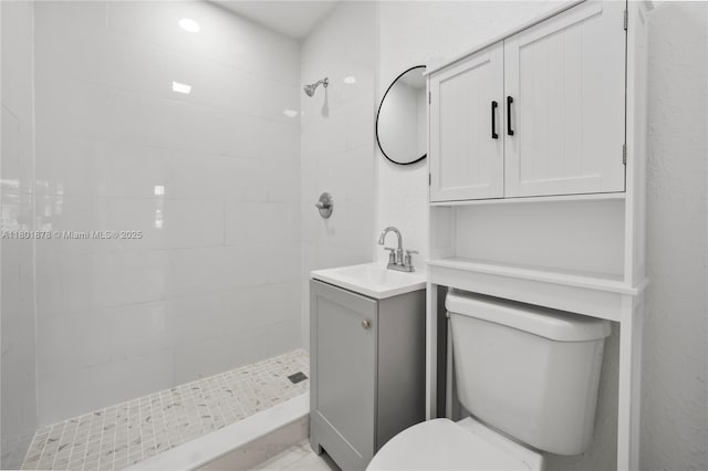 bathroom featuring toilet, tiled shower, and vanity