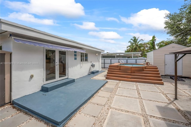 view of patio / terrace with french doors, an outdoor hot tub, a shed, fence, and an outbuilding