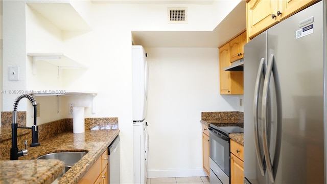 kitchen with stainless steel appliances, a sink, stone counters, under cabinet range hood, and stacked washer / dryer
