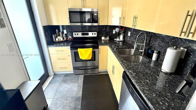 kitchen with stainless steel appliances, a sink, tasteful backsplash, and dark stone countertops