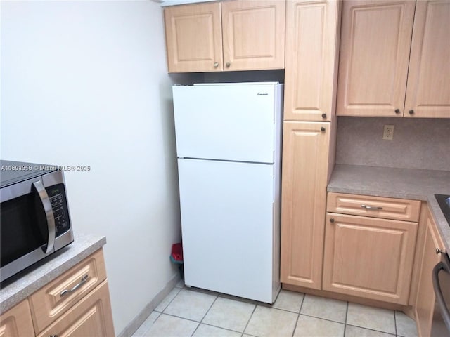 kitchen with freestanding refrigerator, stainless steel microwave, light brown cabinets, light tile patterned floors, and light countertops
