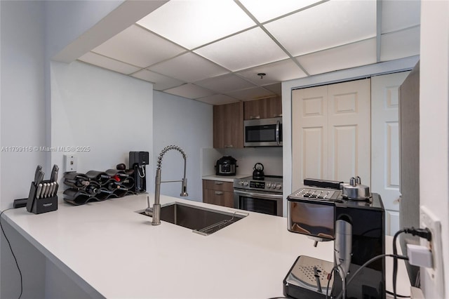 kitchen featuring stainless steel appliances, a sink, light countertops, modern cabinets, and a drop ceiling