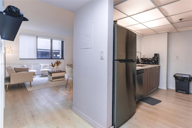 kitchen featuring appliances with stainless steel finishes, light wood-style flooring, light countertops, a sink, and baseboards