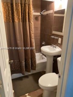 full bathroom with toilet, shower / bath combo with shower curtain, and tile walls