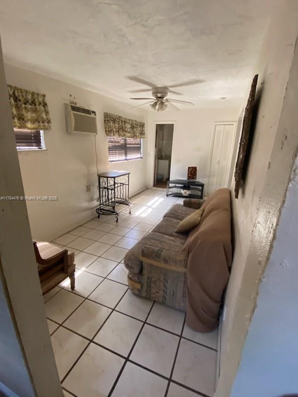 living room with a wall mounted air conditioner, light tile patterned floors, and a ceiling fan