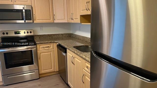 kitchen featuring stainless steel appliances, light wood-style flooring, dark stone counters, and a sink