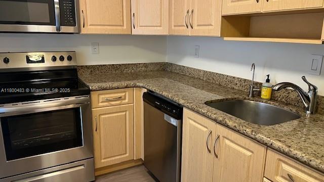 kitchen featuring appliances with stainless steel finishes, a sink, open shelves, and light stone counters