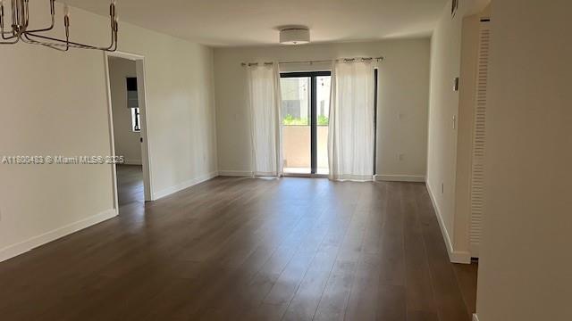 unfurnished room with dark wood-style floors, baseboards, and a chandelier
