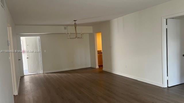spare room with dark wood-style floors, a chandelier, and baseboards