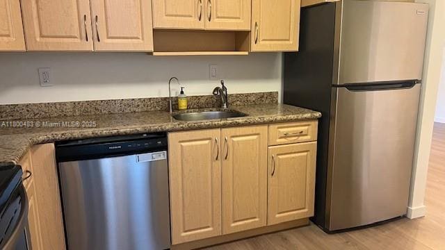kitchen featuring appliances with stainless steel finishes, a sink, light wood-type flooring, dark stone counters, and open shelves
