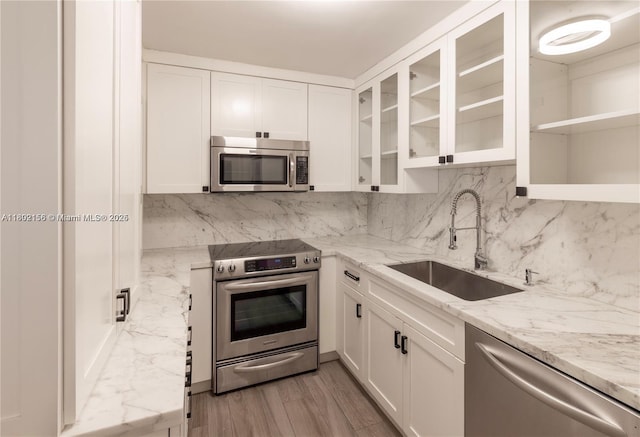 6061 Collins Ave Unit 7D, Miami Beach, FL 33140 - kitchen with appliances with stainless steel finishes, a sink, white cabinets, light stone countertops, and glass insert cabinets