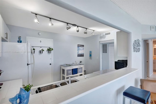 interior space featuring freestanding refrigerator, tile countertops, white cabinets, a kitchen bar, and track lighting