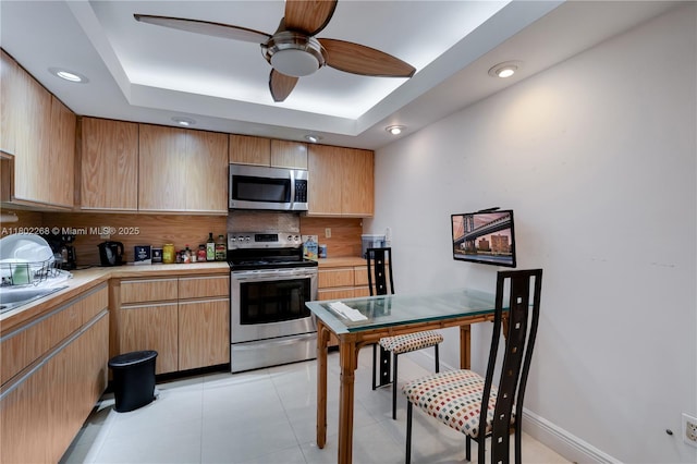 kitchen featuring stainless steel appliances, decorative backsplash, light countertops, a ceiling fan, and a raised ceiling