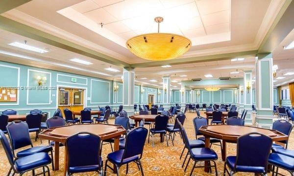 dining space with a decorative wall, a tray ceiling, crown molding, and ornate columns
